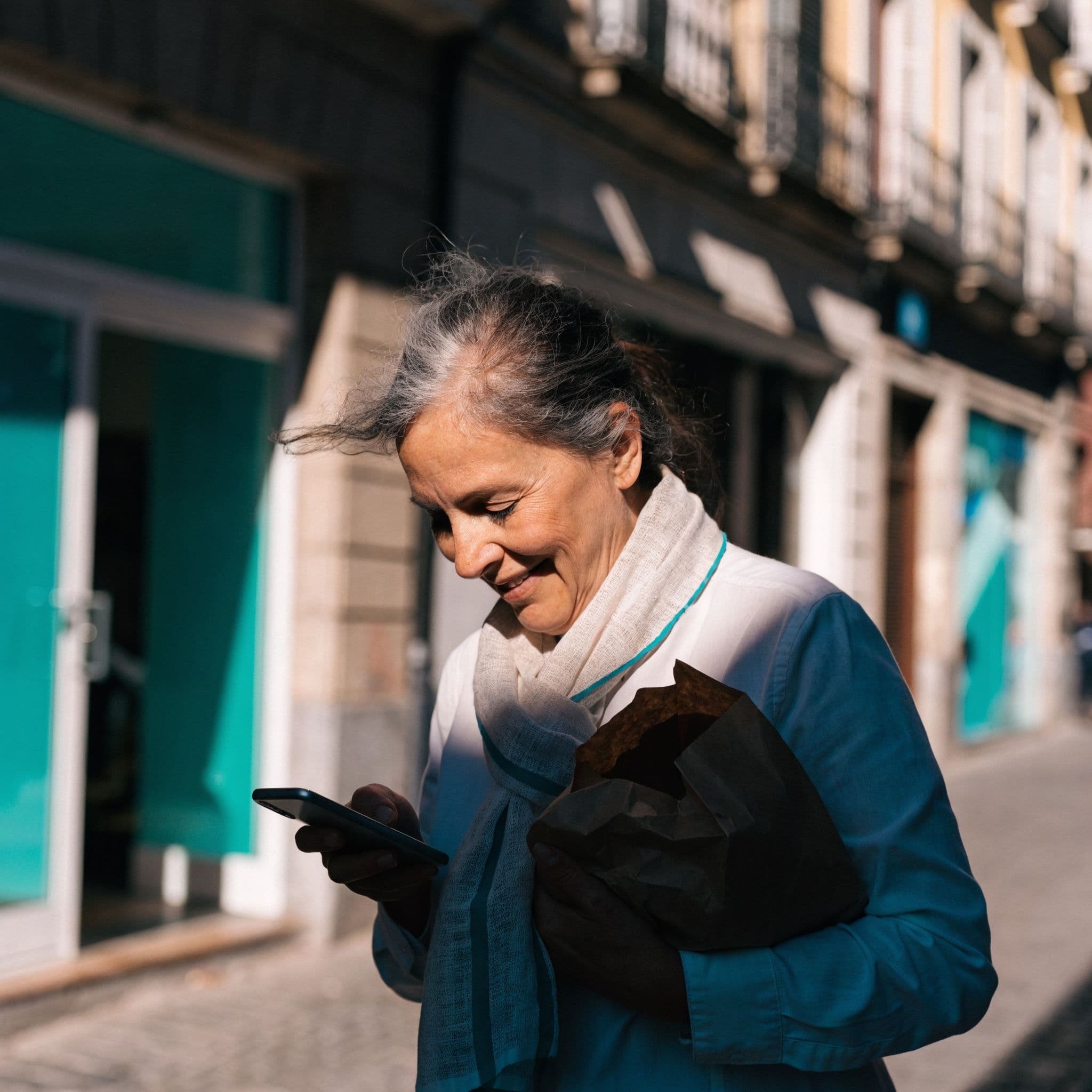 A woman walking home from the bakery smiles at a message on her phone, one that reached her at a good moment.