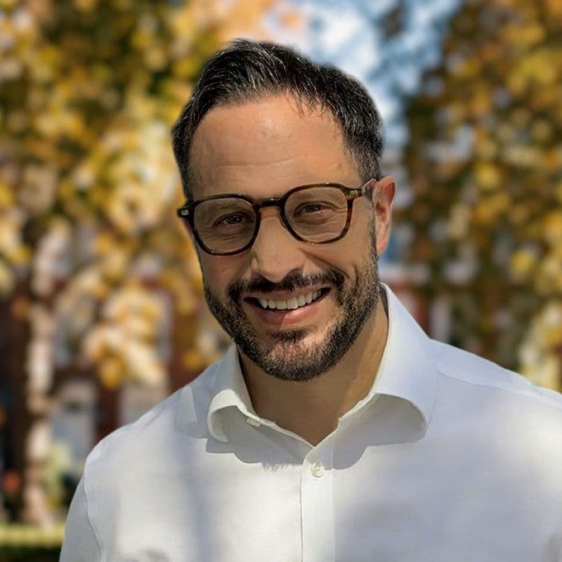 Gareth Evans, Chief Revenue Officer at Intent HQ, smiling in a white shirt in a tree-lined garden square in autumn.